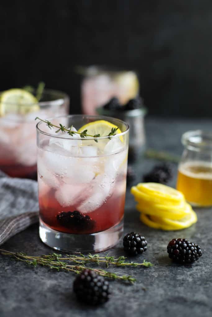 Close up view of a Blackberry-Lemon Thyme Sparkler topped with lemon and fresh thyme. 